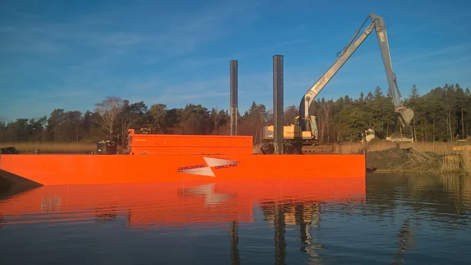 Orange spud barge with Liebherr excavator on winter lake